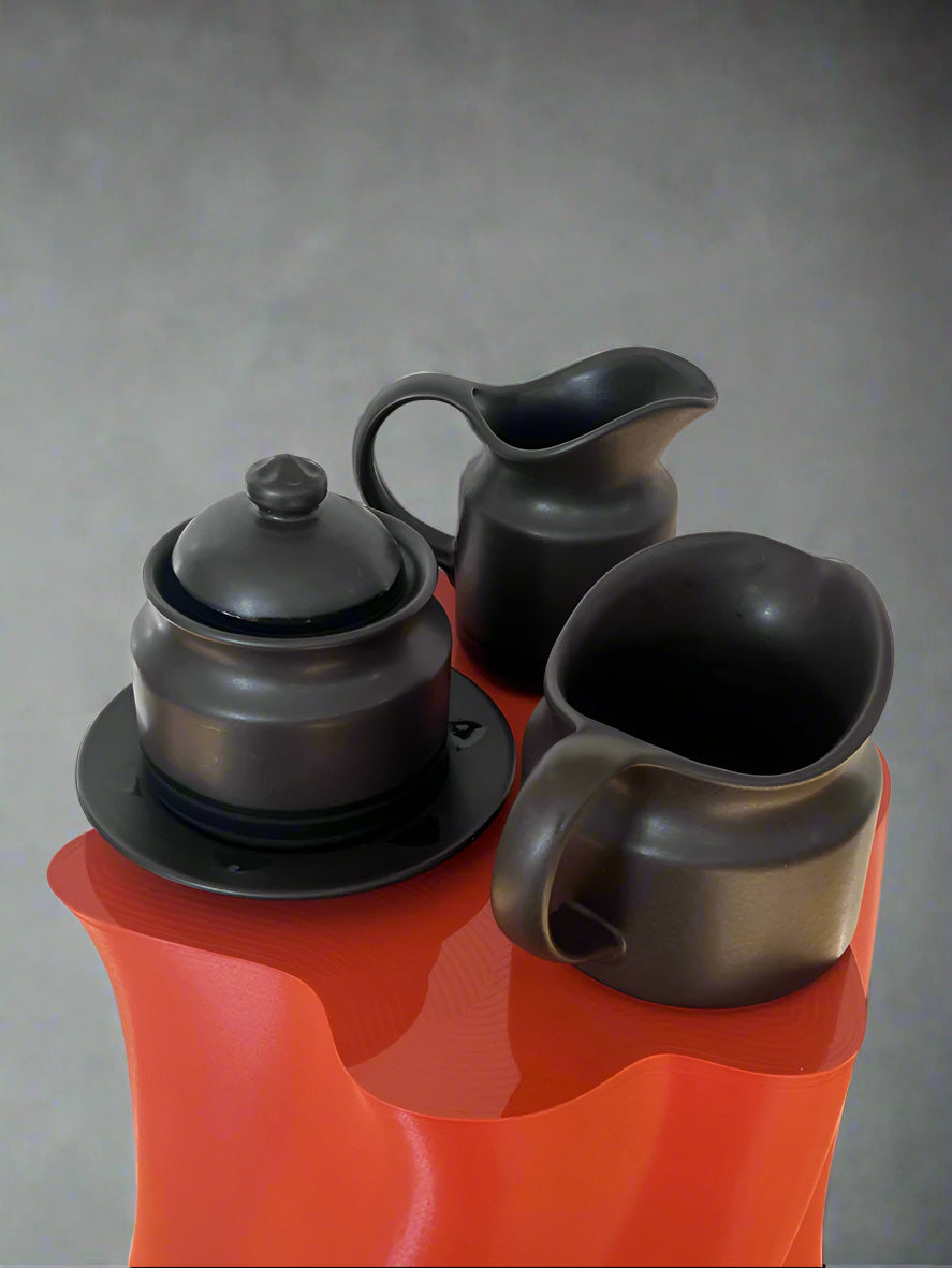 Black ceramic tea set with teapot, milk jug, and cup on a red surface.