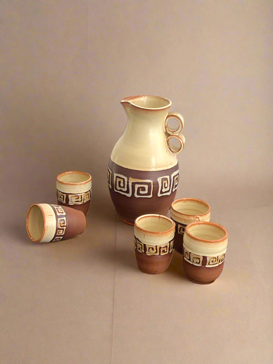 Ceramic pitcher and cups with decorative patterns on a dark surface