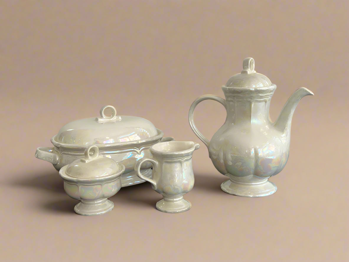 Set of ceramic teaware including a teapot, sugar bowl, and creamer on a black surface with a gray background.