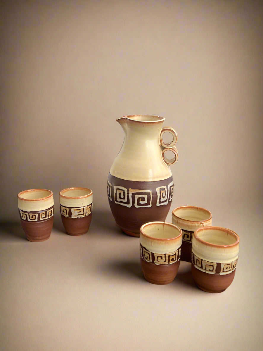 Ceramic pitcher and cups with decorative patterns on a black surface.