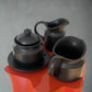 Black ceramic tea set with teapot, milk jug, and cup on a red surface.