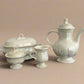 Set of ceramic teaware including a teapot, sugar bowl, and creamer on a black surface with a gray background.