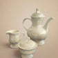 White ceramic tea set on a black surface with a white background